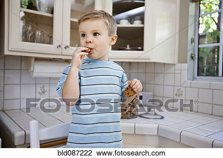 Stock Image - Caucasian boy eating cookie in kitchen. Fotosearch
