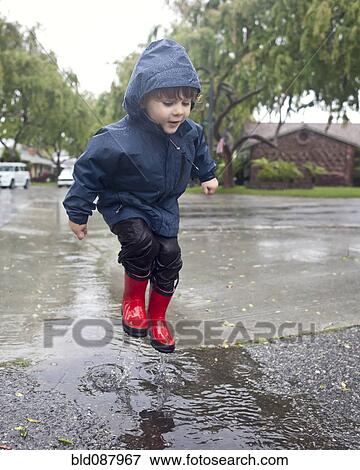 Stock Photo - Caucasian boy jumping in rain puddle. Fotosearch