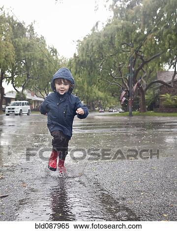 Stock Photography - Caucasian boy splashing in rain puddle. Fotosearch