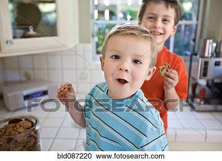 Stock Image - Caucasian brothers sneaking cookies in kitchen. Fotosearch