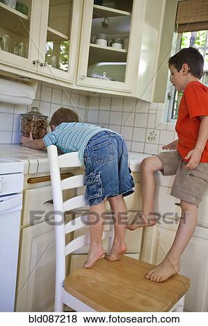 Stock Photo - Caucasian brothers sneaking cookies in kitchen. Fotosearch