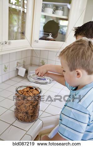 Stock Photo - Caucasian brothers sneaking cookies in kitchen. Fotosearch