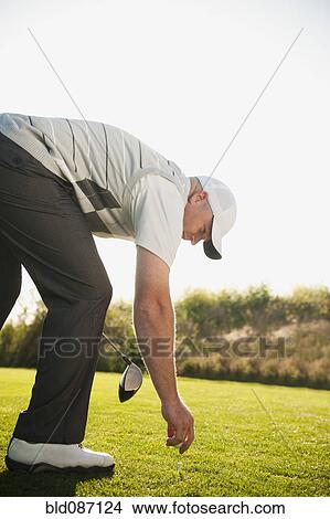 Picture - Caucasian golfer placing ball on golf course. Fotosearch