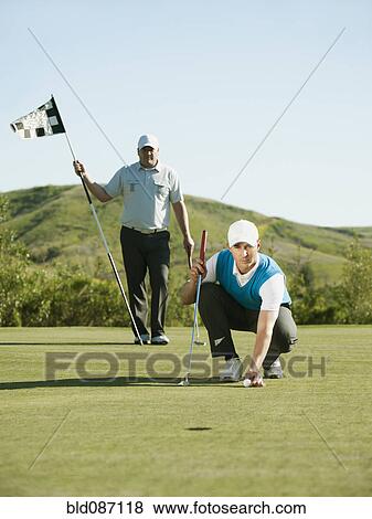 Stock Photo - Caucasian golfer placing golf ball on course. Fotosearch