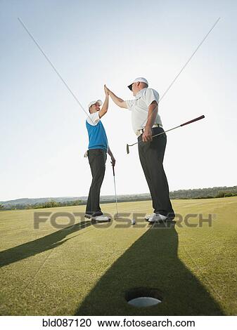 Stock Image - Caucasian golfers high fiving on golf course. Fotosearch