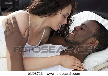 Picture - Couple laying in bed smiling at each other. Fotosearch