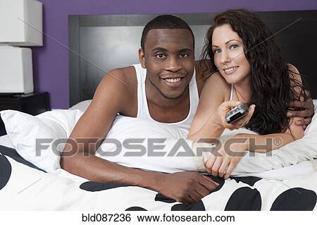 Stock Photograph - Couple laying in bed watching television together. Fotosearch