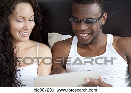 Stock Photography - Couple sitting in bed looking at digital tablet together. Fotosearch