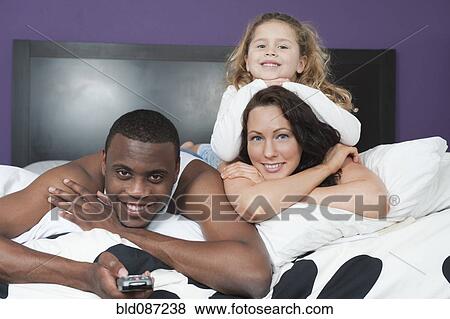 Stock Photo - Family laying in bed together watching television. Fotosearch