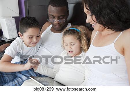 Stock Photo - Family using digital tablet together in bed. Fotosearch