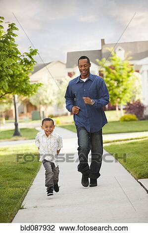 Stock Image - Father and son running on sidewalk. Fotosearch