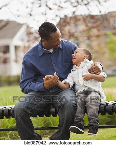 Father and son sitting together on park bench View Large Photo Image Stock Image - Father and son sitting together on park bench. Fotosearch
