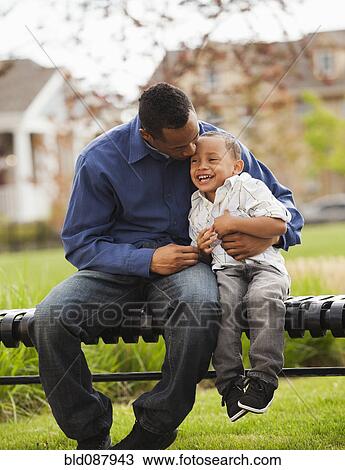 Stock Image - Father and son sitting together on park bench. Fotosearch