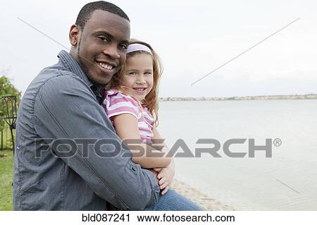 Stock Image - Father hugging daughter at waterfront. Fotosearch
