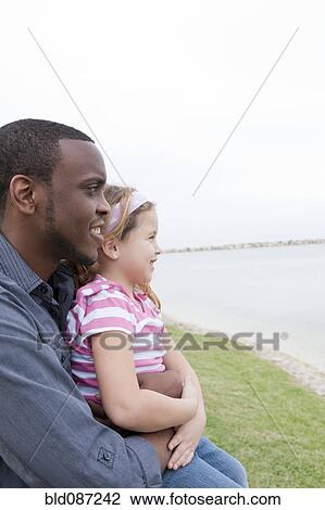 Stock Image - Father hugging daughter at waterfront. Fotosearch