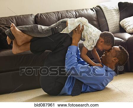 Stock Image - Father playing with son on living room floor. Fotosearch