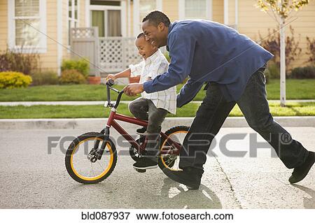 Stock Photo - Father teaching son to ride bicycle. Fotosearch