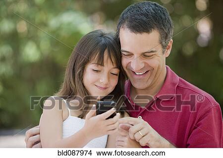 Picture - Hispanic father and daughter text messaging on cell phone. Fotosearch