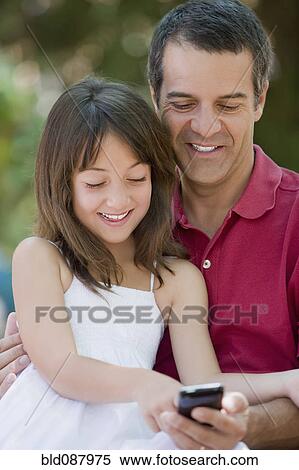 Stock Photography - Hispanic father and daughter text messaging on cell phone. Fotosearch