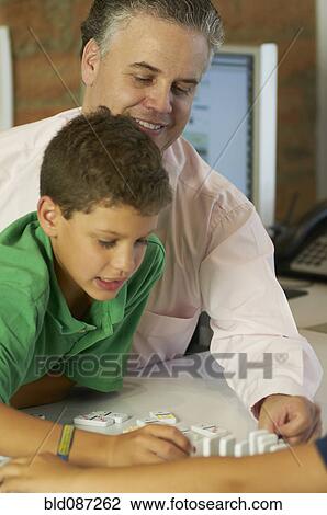 Stock Image - Hispanic father and son playing dominoes. Fotosearch