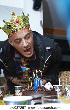 Stock Photo - Hispanic man blowing out candles on birthday cake. Fotosearch
