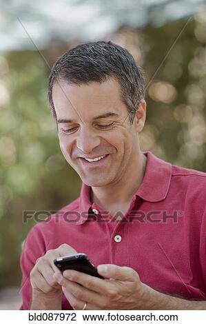 Stock Image - Hispanic man text messaging on cell phone. Fotosearch