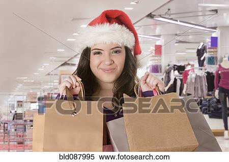 Stock Photography - Hispanic teenage girl in Santa hat holding shopping bags. Fotosearch