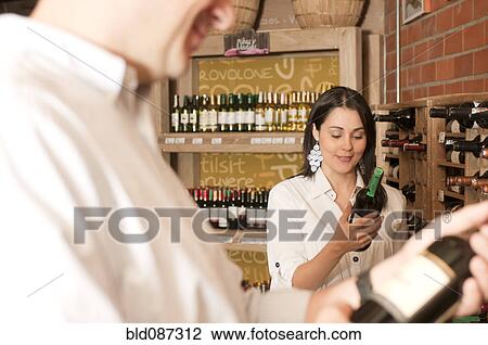 Stock Image - Hispanic woman looking at wine in wine shop. Fotosearch