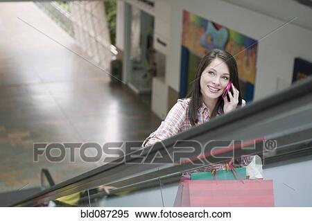 Stock Photography - Hispanic woman on escalator talking on cell phone. Fotosearch