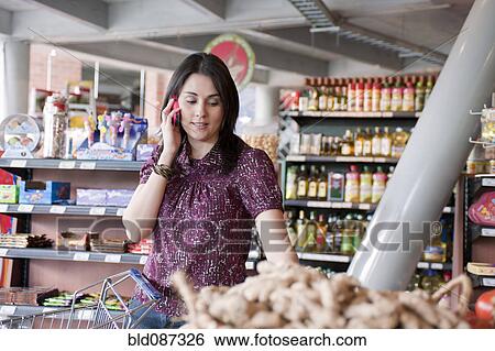 Stock Photograph - Hispanic woman talking on cell phone and shopping in grocery store. Fotosearch