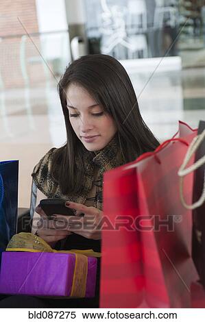 Stock Photography - Hispanic woman with gifts text messaging on cell phone. Fotosearch