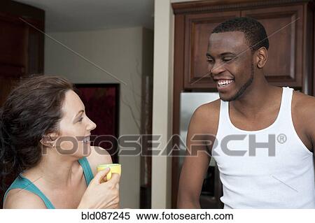 Stock Photography - Husband smiling at wife in kitchen. Fotosearch