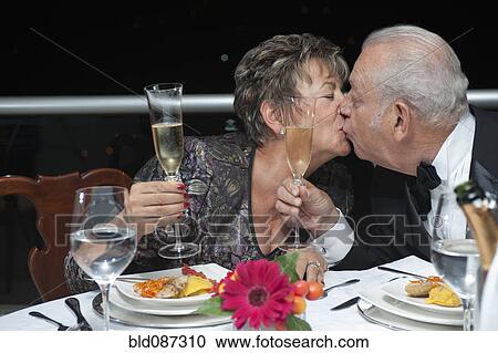 Stock Image - Kissing Hispanic couple toasting with Champagne in restaurant. Fotosearch