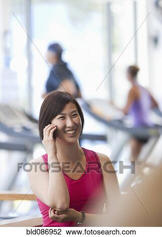 Stock Image - Korean woman talking on cell phone in health club. Fotosearch