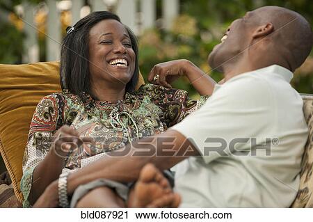 Stock Image - Laughing African American couple sitting outdoors. Fotosearch