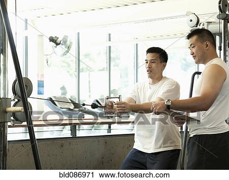 Stock Image - Man working with personal trainer in health club. Fotosearch