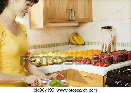 Mixed race woman cutting watermelon in kitchen View Large Photo Image Stock Photo - Mixed race woman cutting watermelon in kitchen. Fotosearch