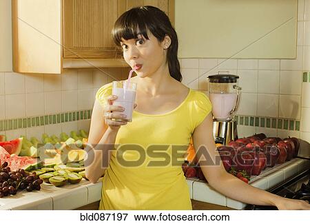Stock Photo - Mixed race woman drinking smoothie in kitchen. Fotosearch