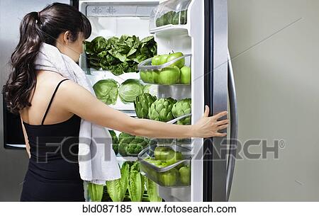 Stock Photography - Mixed race woman looking at green vegetables in refrigerator. Fotosearch