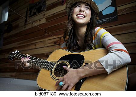 Stock Image - Mixed race woman playing guitar. Fotosearch