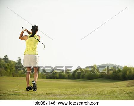 Stock Photograph - Mixed race woman swinging golf club on golf course. Fotosearch