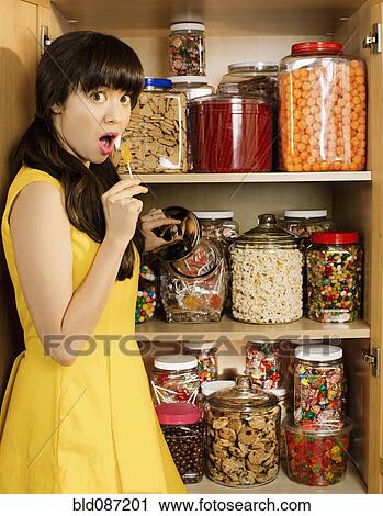 Stock Image - Mixed race woman taking lollipop from cupboard. Fotosearch