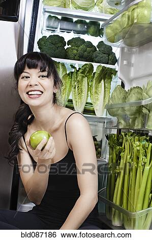 Mixed race woman with apple near green vegetables in refrigerator View Large Photo Image Stock Photograph - Mixed race woman with apple near green vegetables in refrigerator. Fotosearch