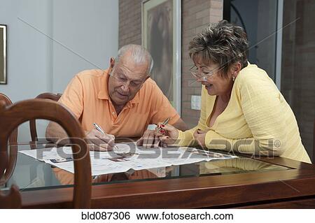 Stock Photograph - Senior Hispanic couple doing crossword puzzle in newspaper. Fotosearch