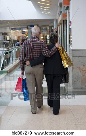 Stock Photo - Senior Hispanic couple hugging and carrying shopping bags. Fotosearch