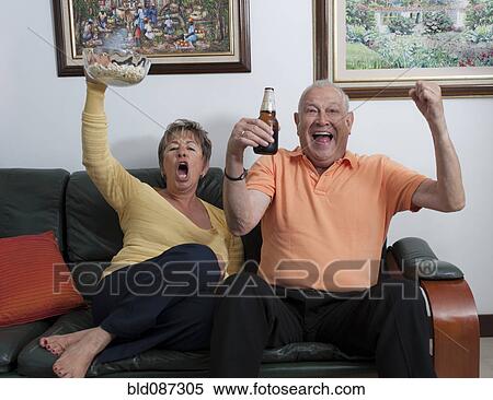 Stock Photography - Senior Hispanic couple watching television and cheering. Fotosearch