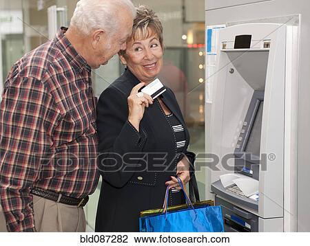 Stock Image - Senior Hispanic couple withdrawing money from ATM. Fotosearch
