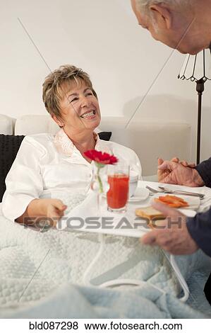Stock Photo - Senior Hispanic man bringing wife breakfast in bed. Fotosearch