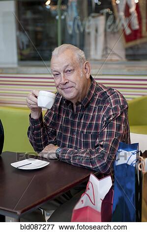 Stock Photo - Senior Hispanic man drinking coffee in cafe. Fotosearch
