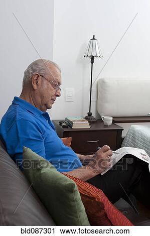Senior Hispanic man sitting on sofa looking at newspaper View Large Photo Image Stock Image - Senior Hispanic man sitting on sofa looking at newspaper. Fotosearch